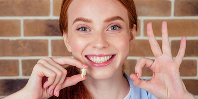 Redhead girl smiling and holding her removed wisdom tooth
